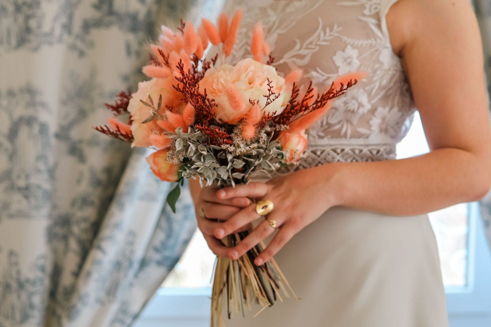 Le bouquet de la mariée, roses pêche et feuillages, tenu contre la robe.
