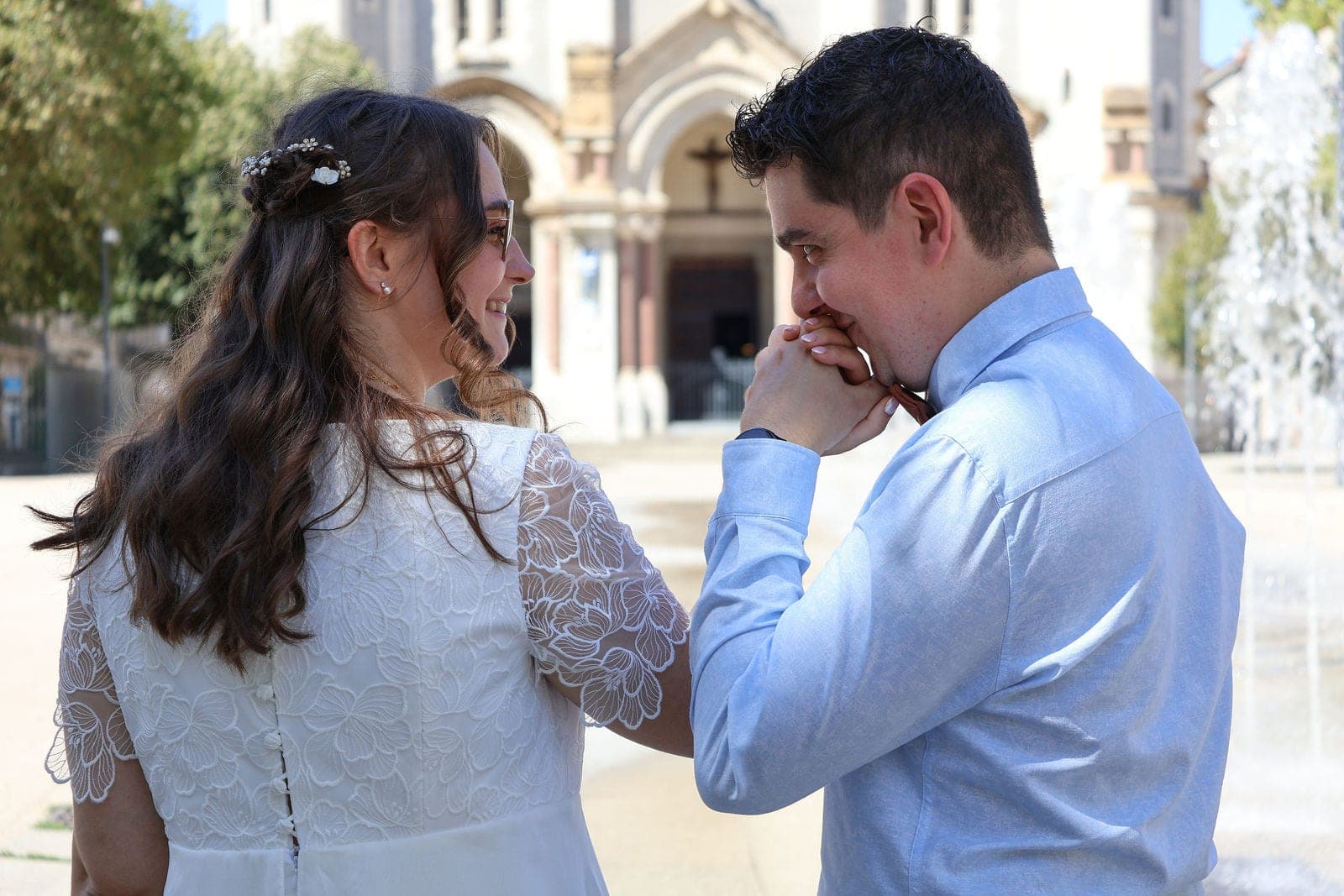 Le marié embrasse la main de la mariée, devant la fontaine.