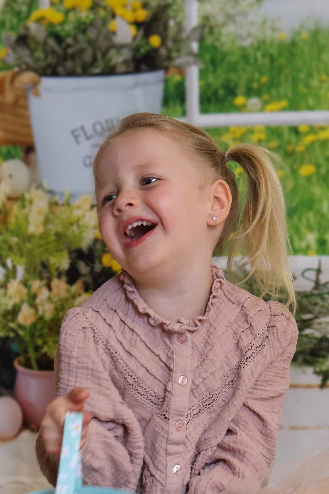 Une petite fille éclate de rire devant le décor fleuri du studio.