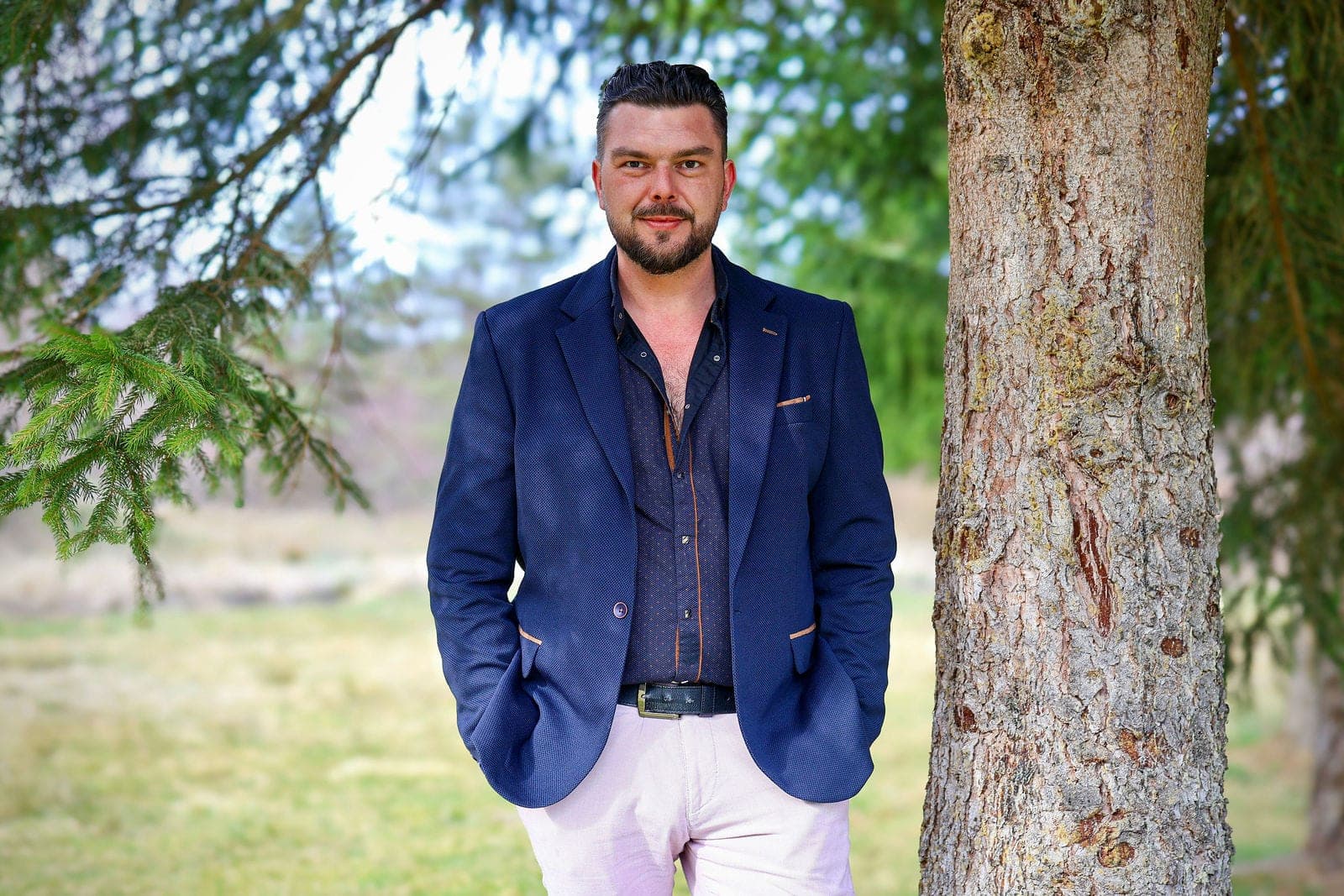 Portrait d’un homme en veste bleue, adossé à un arbre.