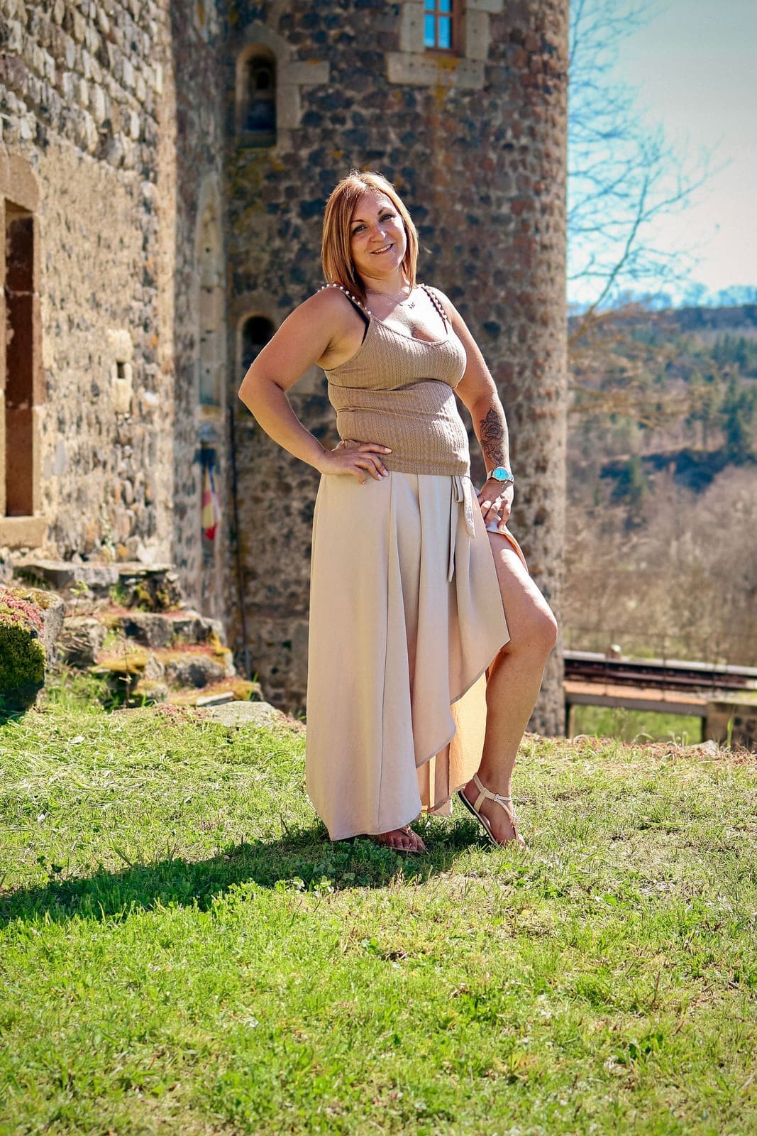 Une femme en robe longue beige, devant la tour de pierre.
