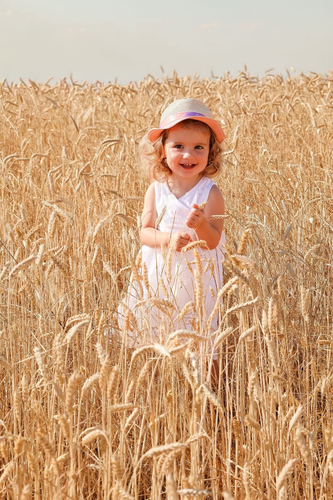 Une petite fille en robe blanche et chapeau, au milieu des épis.