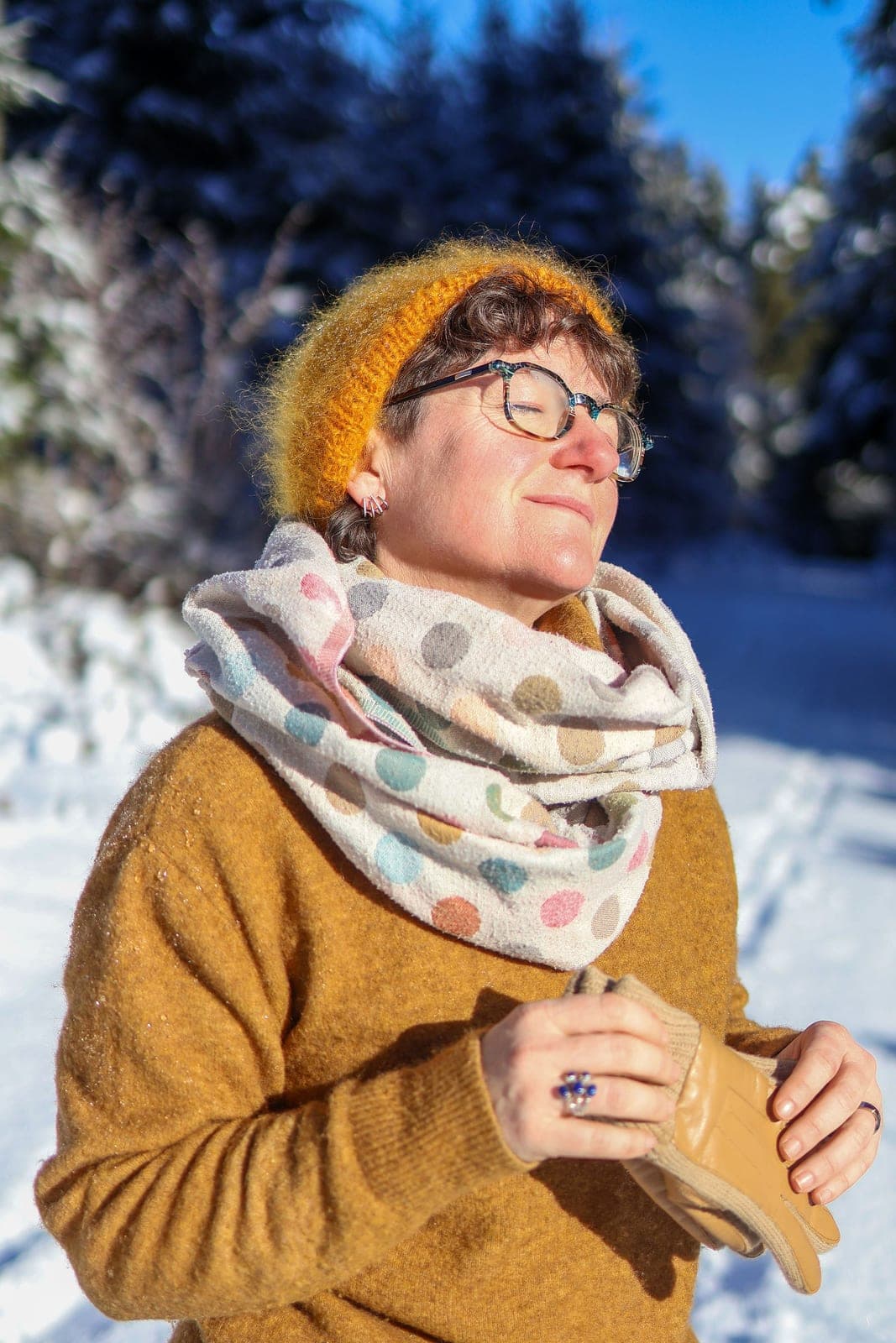 Une femme en pull moutarde et bonnet, dans la neige, en plein soleil d’hiver.