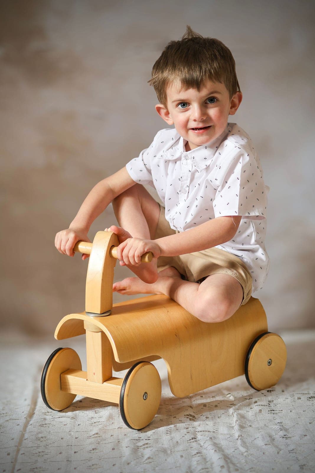 Un tout-petit sur son porteur en bois, au studio.