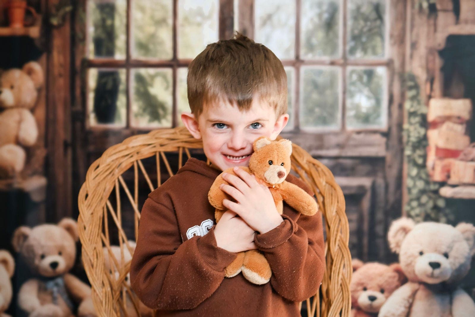 Un garçon serre son ourson, entouré de peluches, dans le fauteuil en osier.