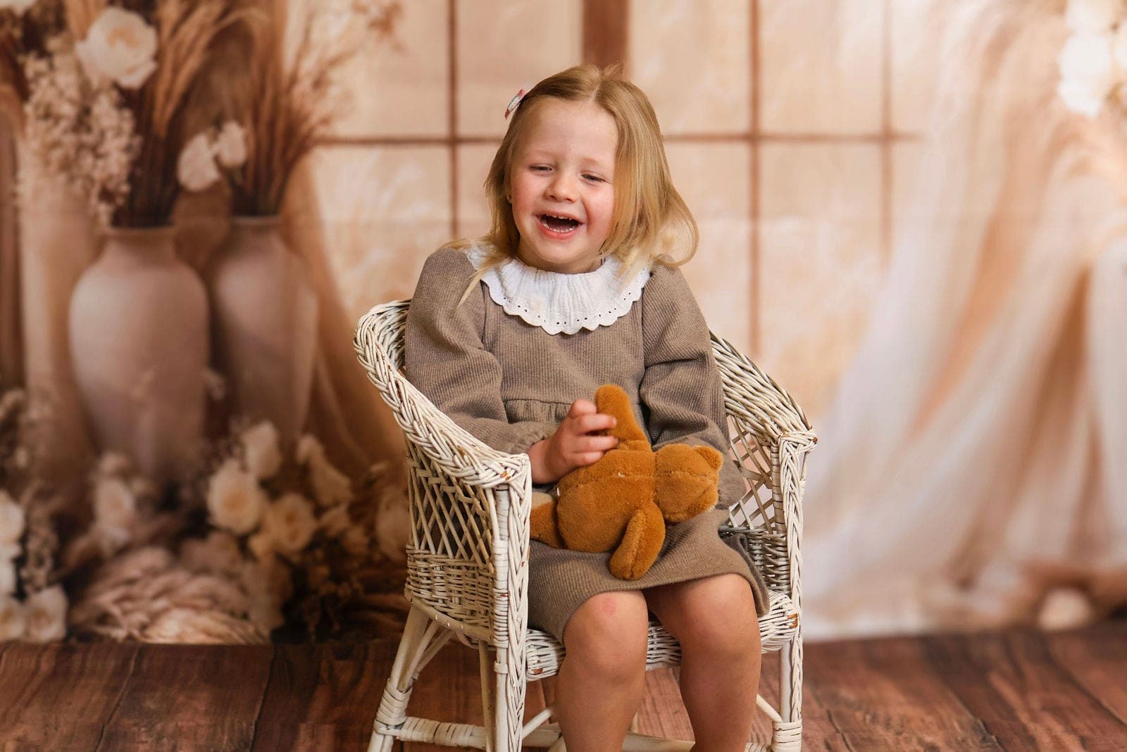 Une petite fille rit aux éclats dans son fauteuil en osier, son doudou sur les genoux.