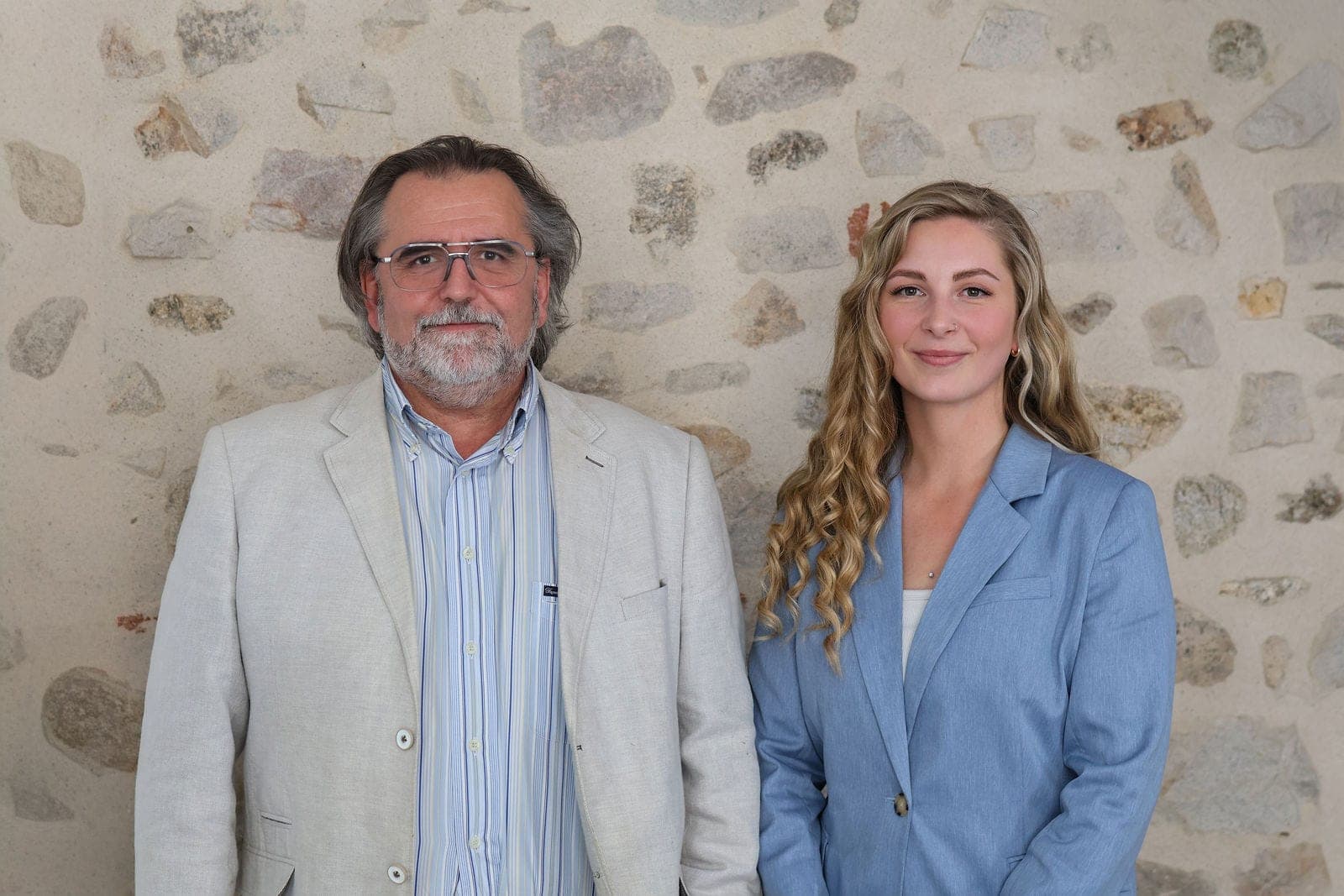 Deux collaborateurs posent ensemble devant le mur de pierre.