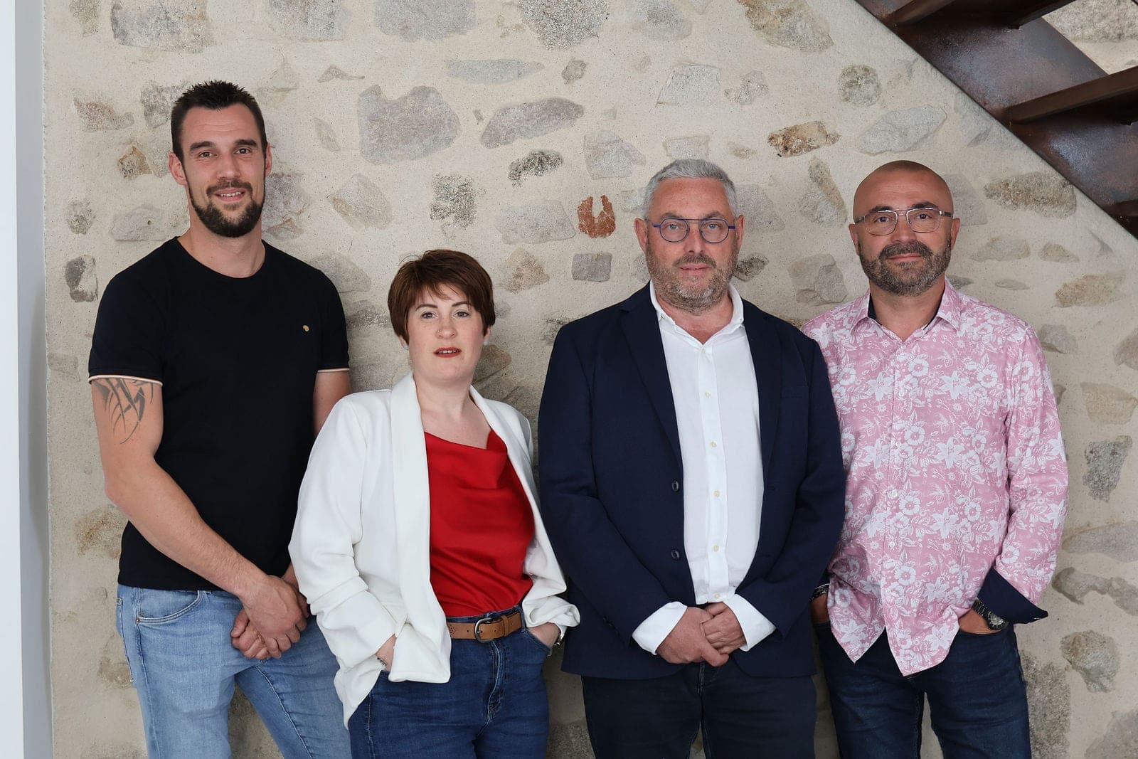 Quatre collègues alignés devant le mur de pierre du bureau.