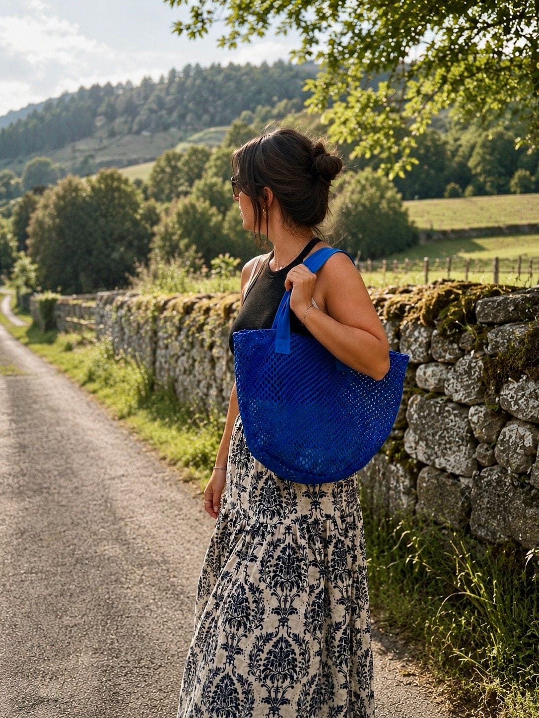 Un sac cabas bleu porté sur un chemin de campagne, entre les murets de pierre.